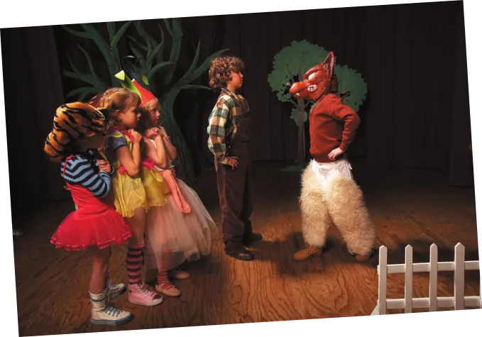 Imagem de crianças interpretando personagens em uma peça de teatro. Uma delas usa figurino de lobo e está diante de um menino. Atrás dele, três meninas estão em fila.