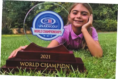 Imagem de Bella Simões. Ela está deitada de bruços em um gramado e segura um troféu.