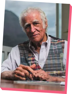 Imagem de Ziraldo. Ele é idoso, usa um colete xadrez e está com as mãos apoiadas sobre uma mesa.