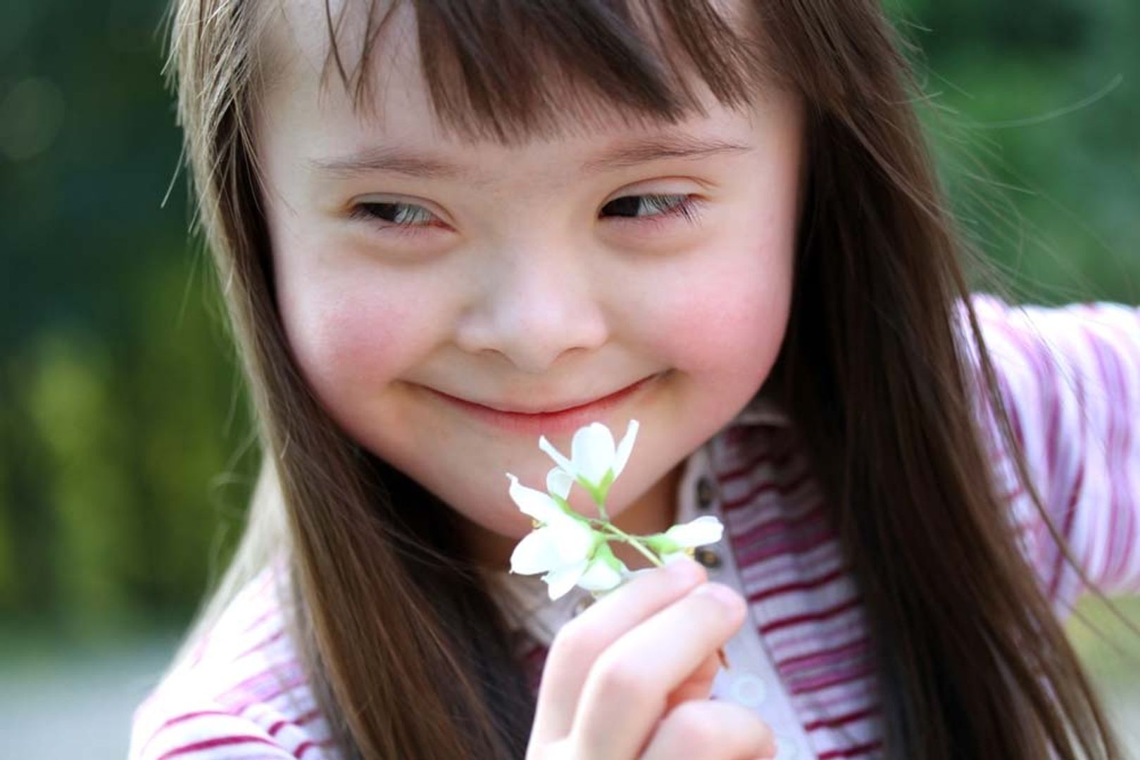 Foto de uma criança com síndrome de down sorrindo com uma flor na mão.