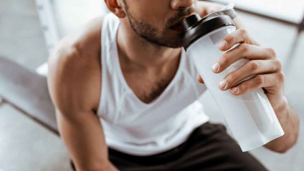 man drinking from a shaker bottle during a workout