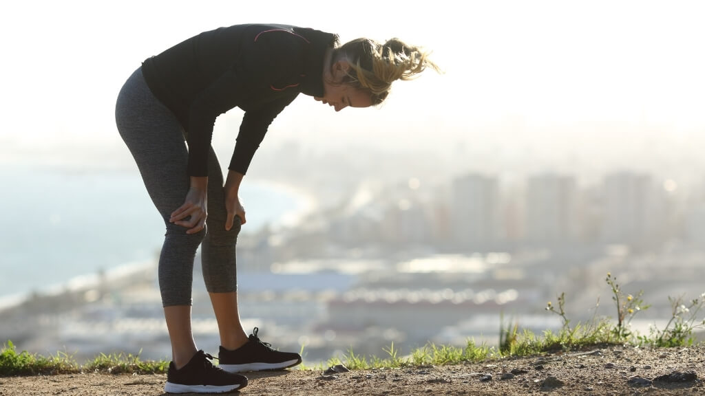 A dehyrated young woman at top of a hill she ran up to