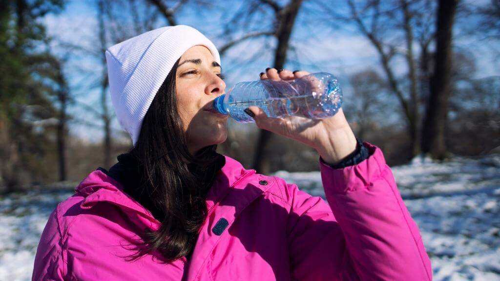 Woman drinking water to stay hydrated during a winter hike in snow