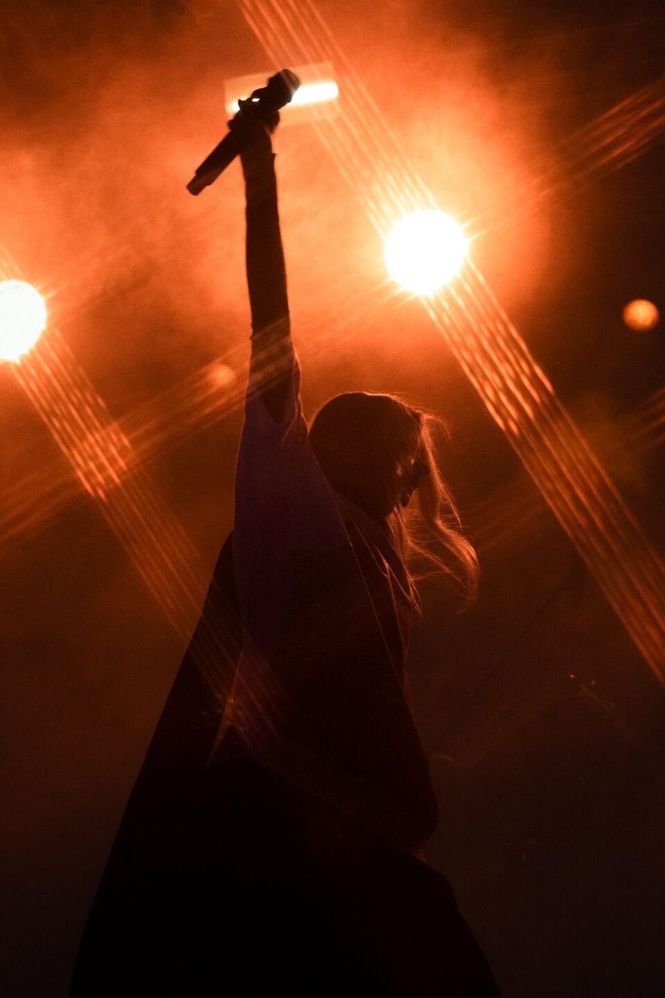 A singer silhouetted against orange stage lights, raising a microphone overhead