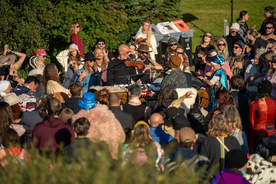 A violinist playing in the middle of a dancing crowd on the grass, people close on every side