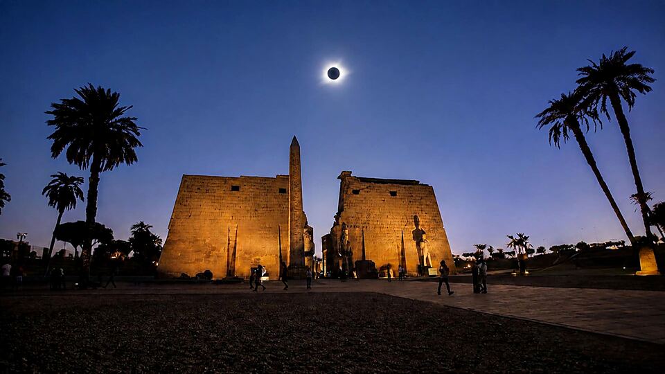 Totality above the lit pylons of Luxor Temple at dusk