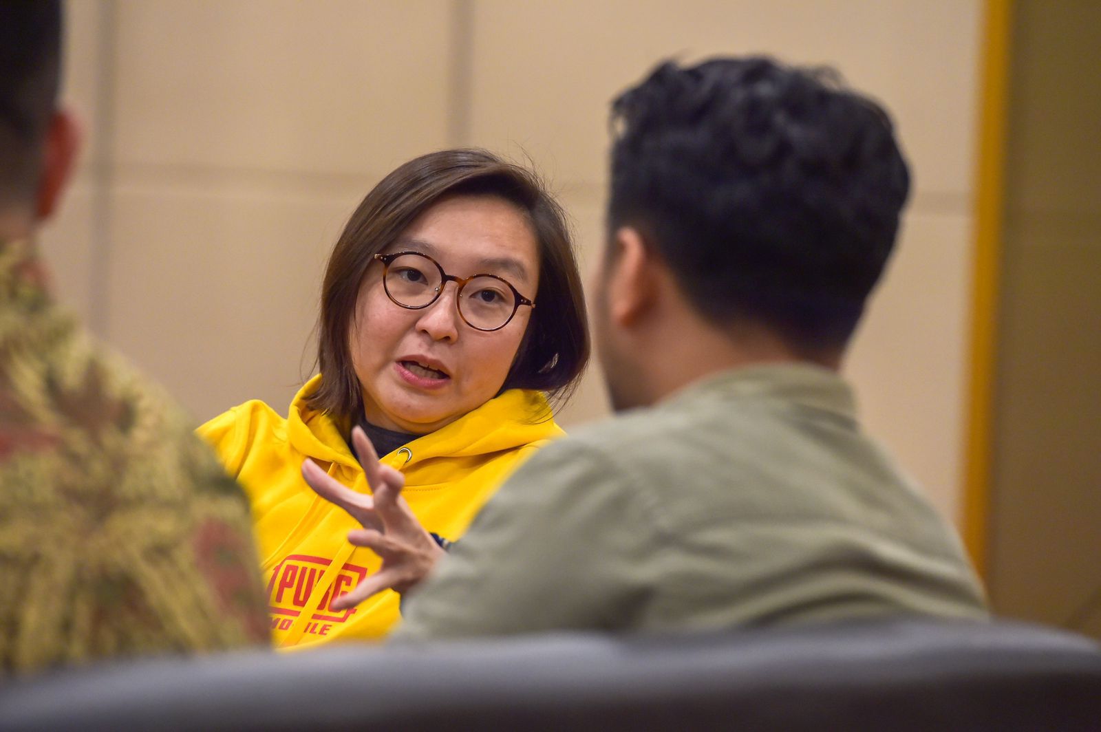 A person in a yellow hoodie is engaged in conversation, gesturing while speaking to another individual in a casual setting.