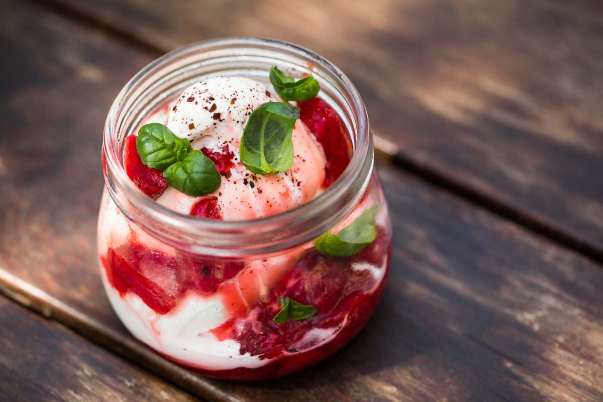 frozen yoghurt with strawberries, sumac and basil in a mason jar set on a wood table