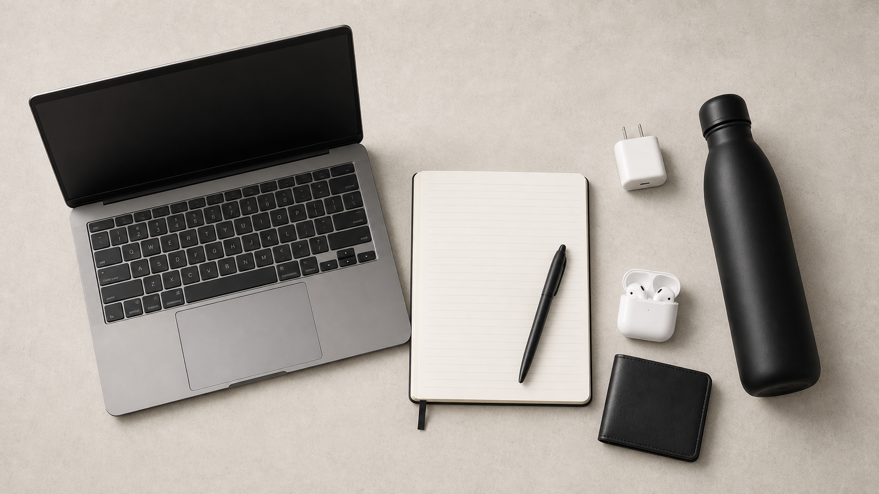 Campus essentials flat lay — laptop, notebook, charger, water bottle, earbuds, wallet on concrete surface