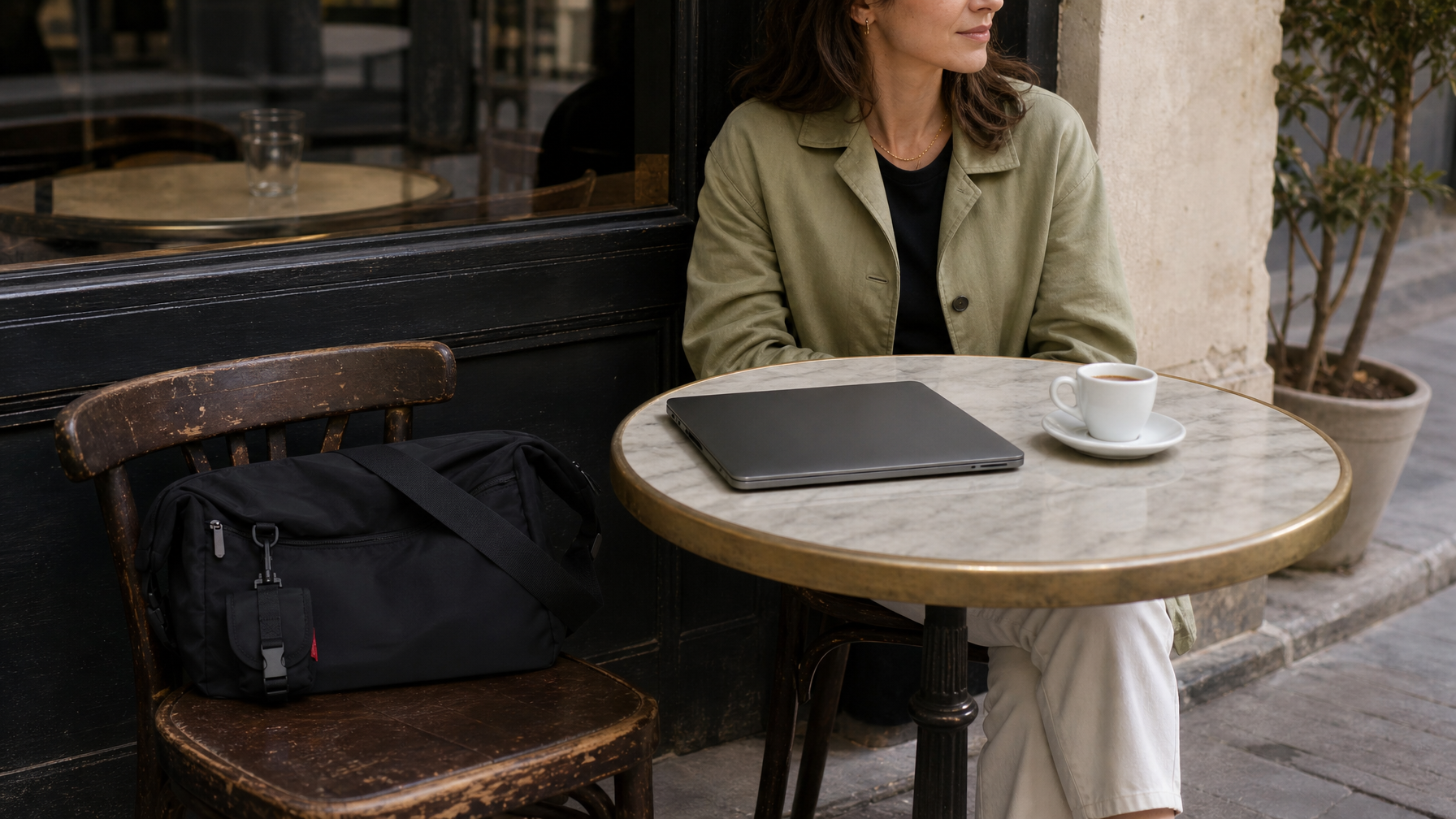 Cafe table with a closed laptop, espresso, and a black messenger on the chair after a walk