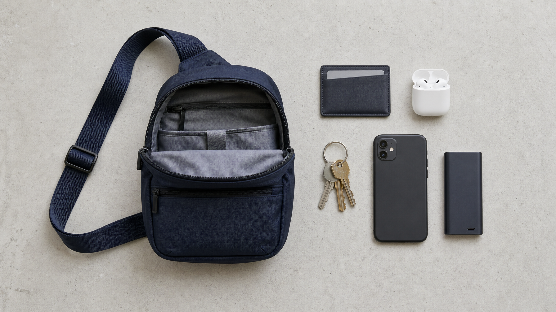 Overhead flatlay of an open sling bag with everyday carry items arranged beside it