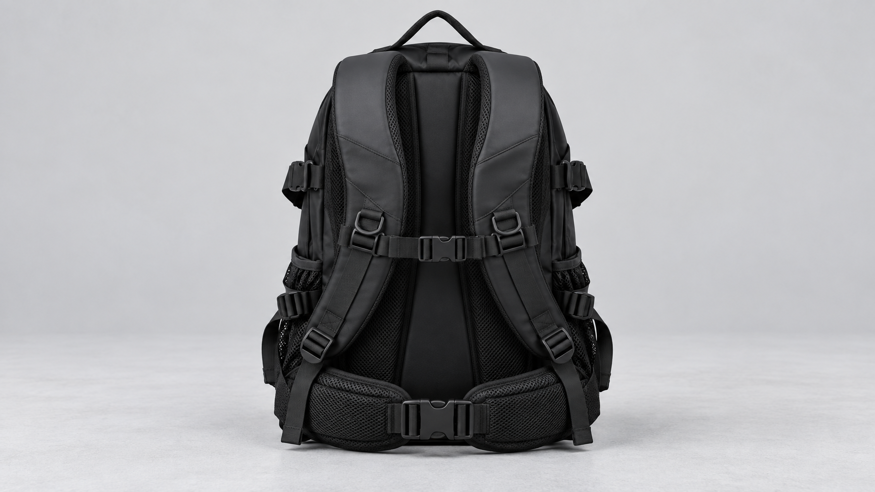 Back panel of a closed black Apex backpack showing S-shaped padded shoulder straps, air-cushion waist belt, and chest buckle on a light gray surface