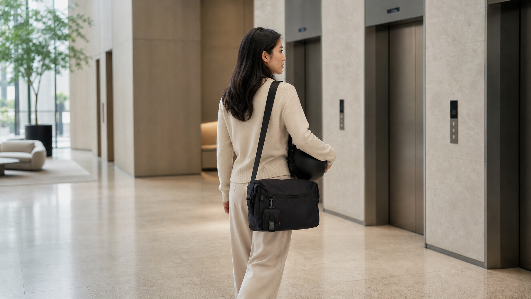 Office lobby arrival with helmet under one arm and a closed black messenger at the side