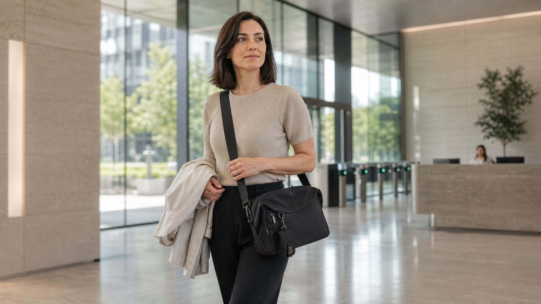 Professional arriving in a bright office lobby after a walking commute with a black messenger bag