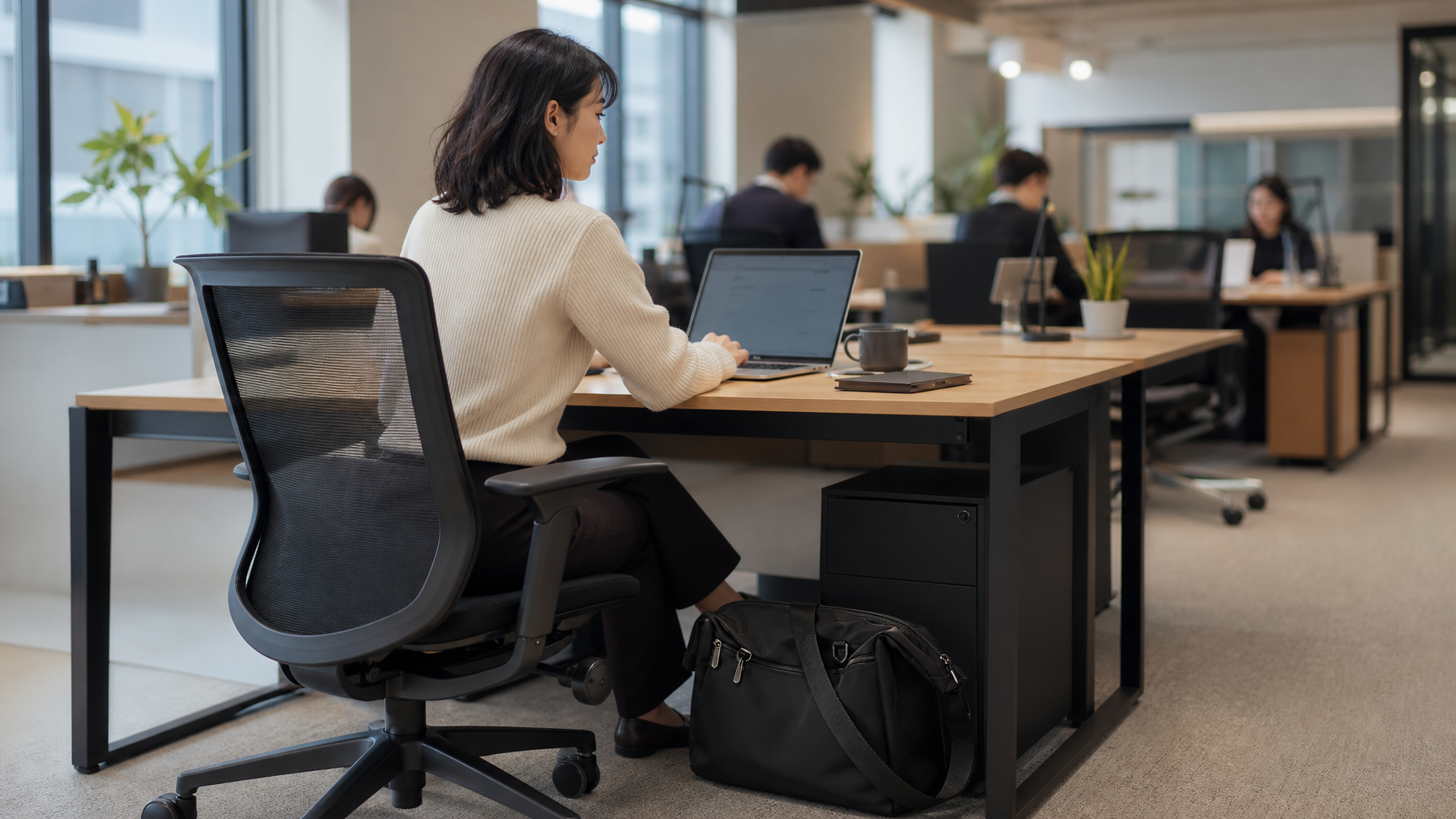 Woman working at co-working hot desk with structured messenger bag on floor beside chair