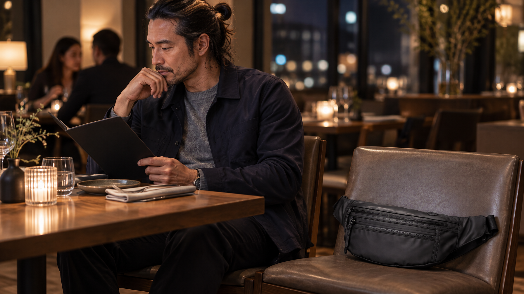 Professional in navy jacket at a restaurant table with a compact black waist pack nearby while reading a menu