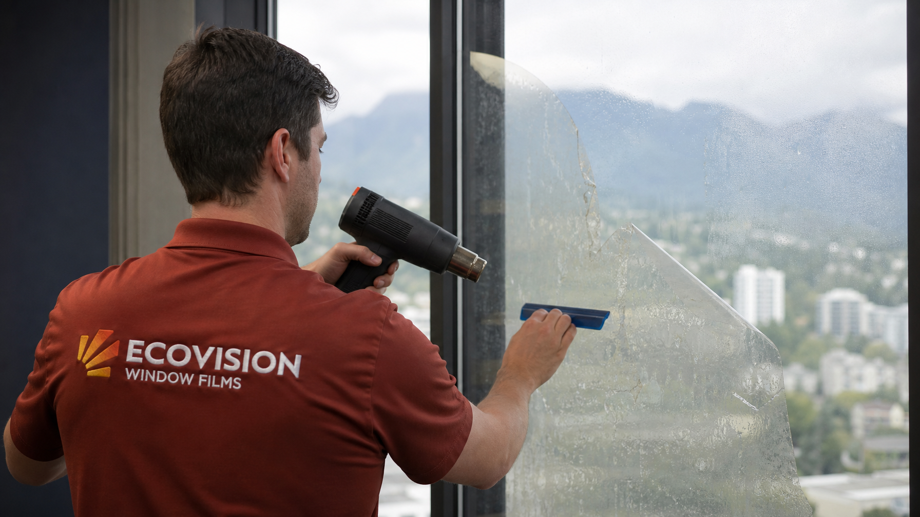 Ecovision installer in brick-red work shirt using a heat gun and plastic scraper to remove aged window film from a Vancouver office building glass facade