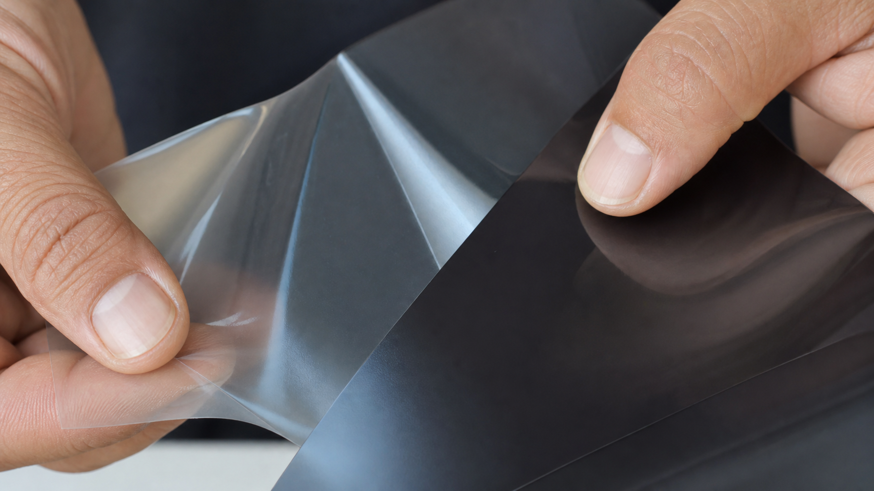 Close-up detail of installer hands releasing the adhesive liner from security window film