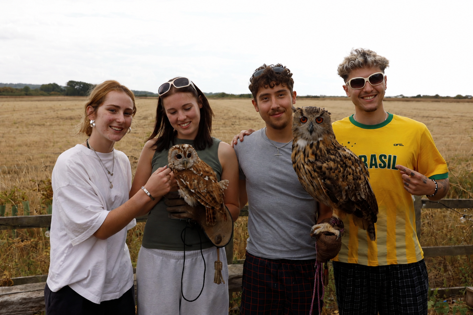 Four young guests smiling in a North Norfolk field holding a tawny owl and an eagle owl on falconry gloves during an Owls About owl handling experience, UK