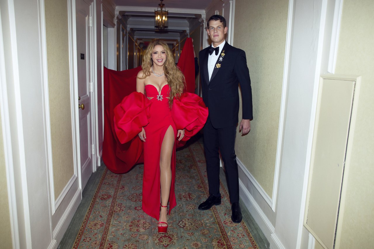 Shakira wears a strapless crepe column gown in signature Herrera Red with a sculptural rose-shaped cape in silk gazar. To accessorize the look, Shakira carries a Herrera Red silk satin draped clutch.