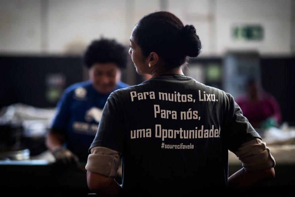 Cooperada da Cooperativa Recifavela usando uma camiseta com a frase “Para muitos, lixo. Para nós, uma oportunidade!”. As cooperativas de reciclagem são responsáveis pela coleta e triagem dos resíduos pós-consumo, tendo como fonte de renda os resíduos pós-consumo descartados pelos consumidores.