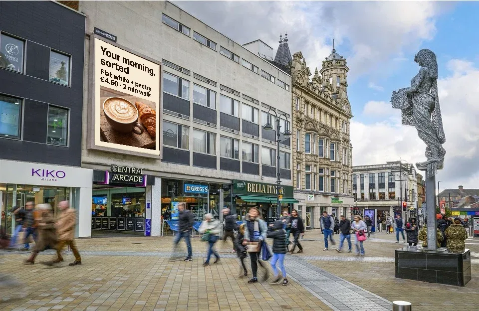 Example portrait coffee shop ad reading Your morning, sorted, on a digital screen above shops on Briggate, Leeds