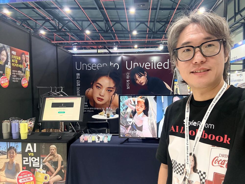 StyleRoom CEO Oh Hyun-seok in front of the booth, with the game monitor and campaign banners behind him
