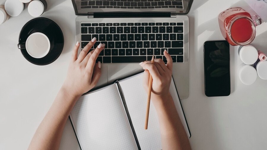 Jasa penulis artikel profesional mengerjakan proyek menulis di laptop dan buku catatan