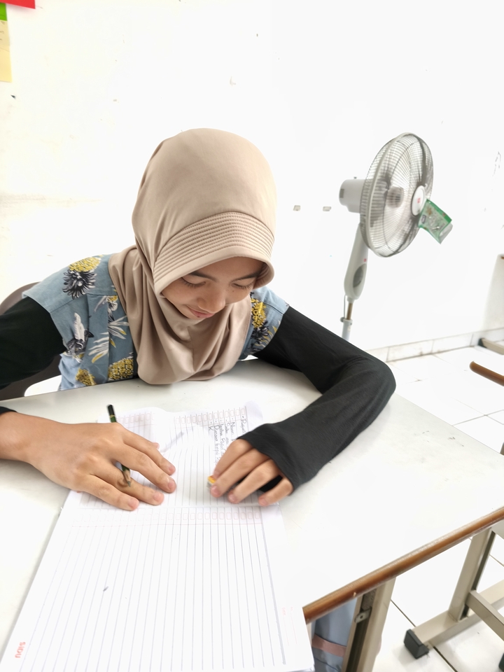 Siswa perempuan berhijab belajar di kelas online dengan membuka buku dan memegang pensil.