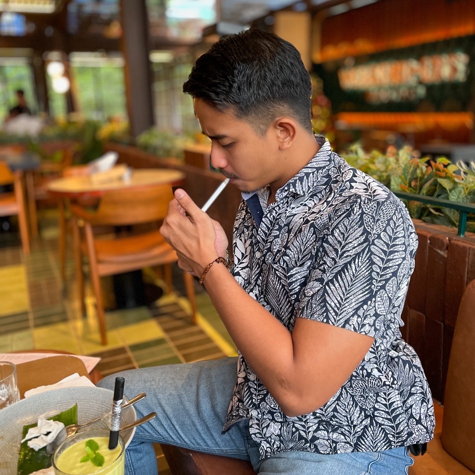 Jasa endorse selebgram murah, selebgram pria tampan dengan kaos hitam putih sedang merokok dan minum kopi.