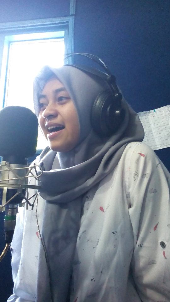 Pengisi suara wanita berhijab sedang melakukan rekaman voice over untuk iklan.