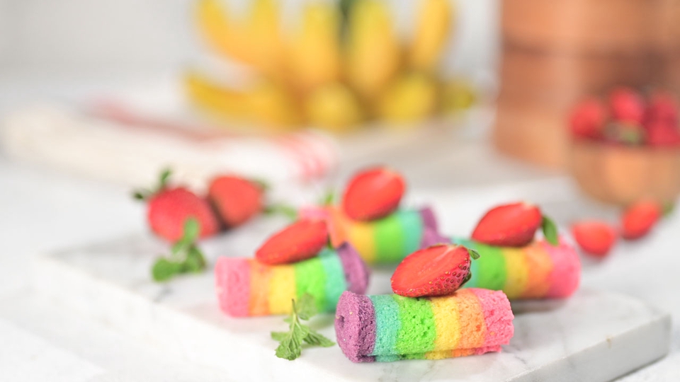 Jasa fotografi makanan dengan background putih, menampilkan cake roll pelangi dengan topping strawberry. Ideal untuk promosi jasa foto produk makanan dan makanan online.