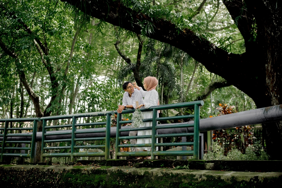 Jasa fotografi prewedding pasangan di taman dengan latar belakang pepohonan hijau.