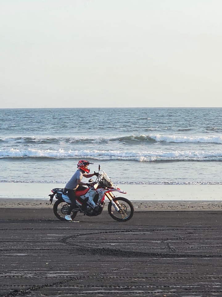 Seorang pria sedang mengendarai motor di pantai, menikmati perjalanan sambil menikmati angin laut.