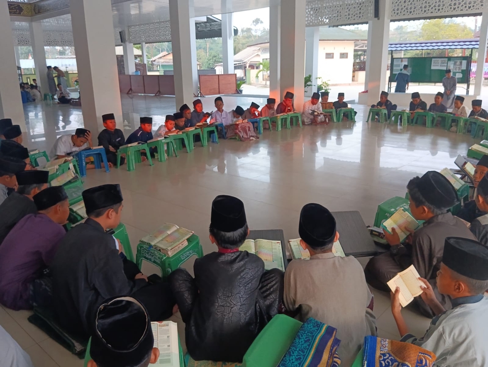 Sejumlah pelajar duduk bersila di lantai dan mempelajari buku. Beberapa di antaranya berdiskusi tentang topik pelajaran, dengan sebagian yang lainnya mendengarkan dengan saksama.