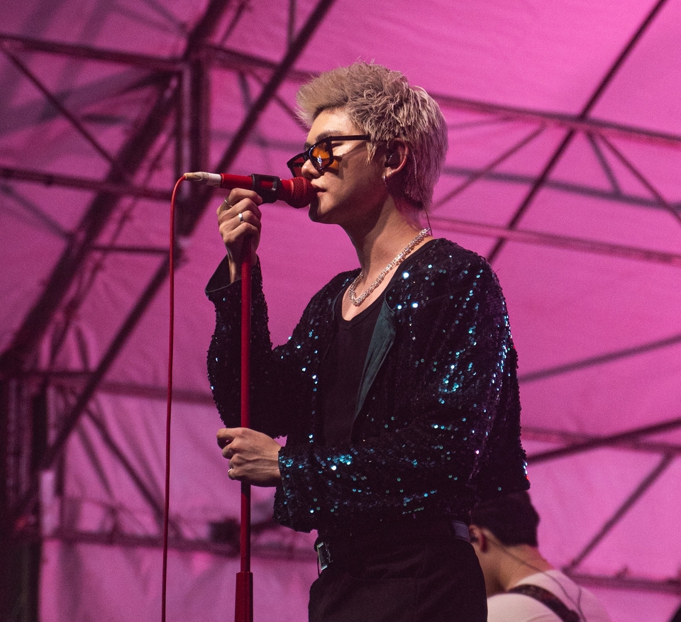 ช่างภาพชายใส่แว่นกันแดดกำลังร้องเพลงบนเวที