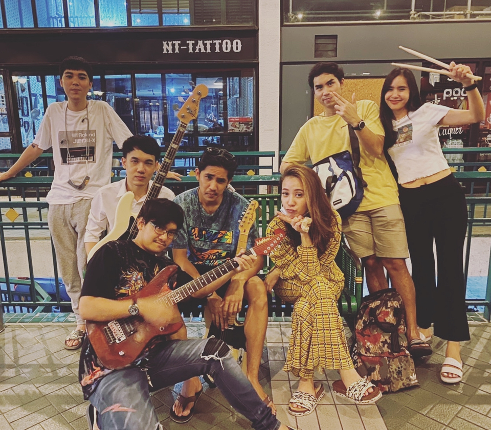 กลุ่มนักดนตรีไทยกำลังทำดนตรีด้วยกัน มีกีต้าร์ไฟฟ้า กลอง และไมโครโฟน