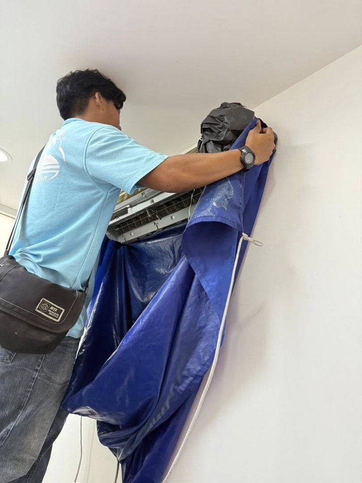 ช่างล้างแอร์กำลังล้างแอร์บ้านด้วยผ้าคลุมเครื่องปรับอากาศ