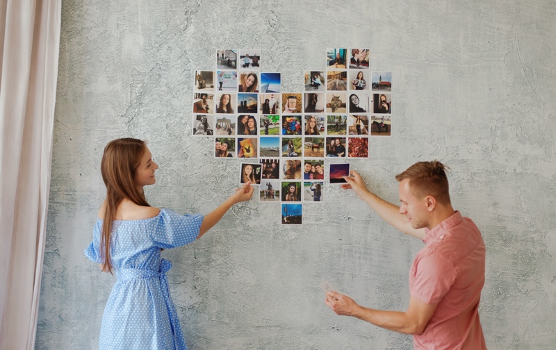 A Couple pasting pictures on a wall to form a heart.