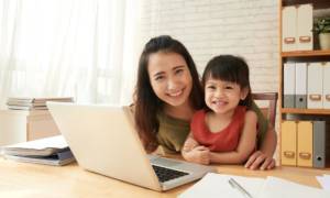 Happy female entrepreneur sitting at office table with her little daughter
