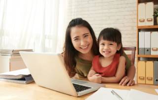 Happy female entrepreneur sitting at office table with her little daughter