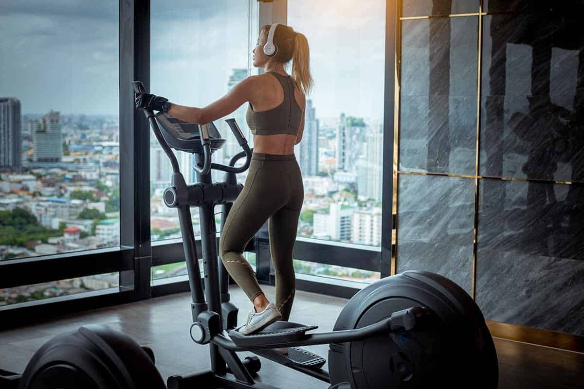 Young fitness sport woman using an elliptic machine trainer at gym fitness center, listening a music with headphones, machine aerobic for slim and firm healthy lifestyle.