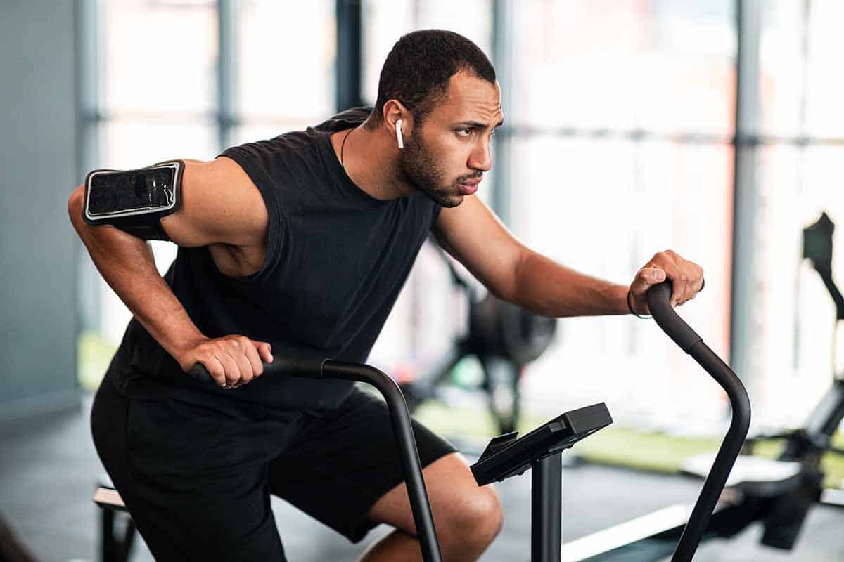 Motivated Black Man Making Cardio Training With Elliptical Bike Machine At Gym, Sporty African American Guy Exercising In Modern Fitness Studio, Enjoying Healthy Lifestyle, Closeup With Free Space