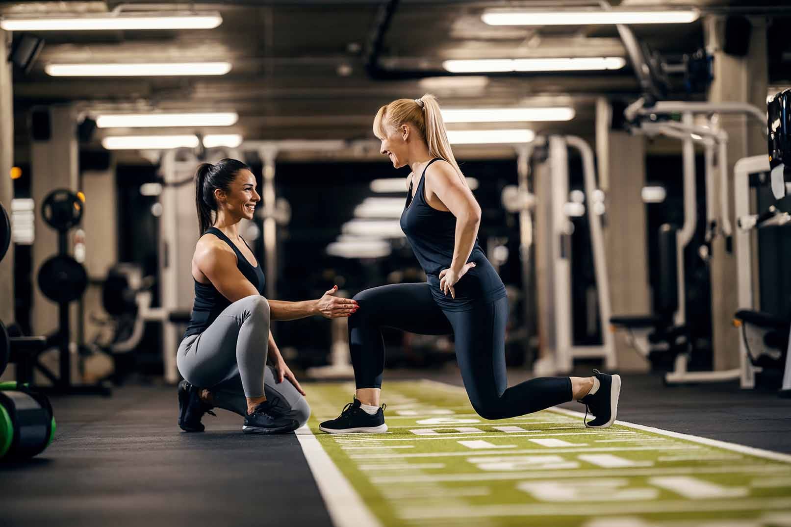 A female trainer is helping sportswoman to do exercises in a gym.