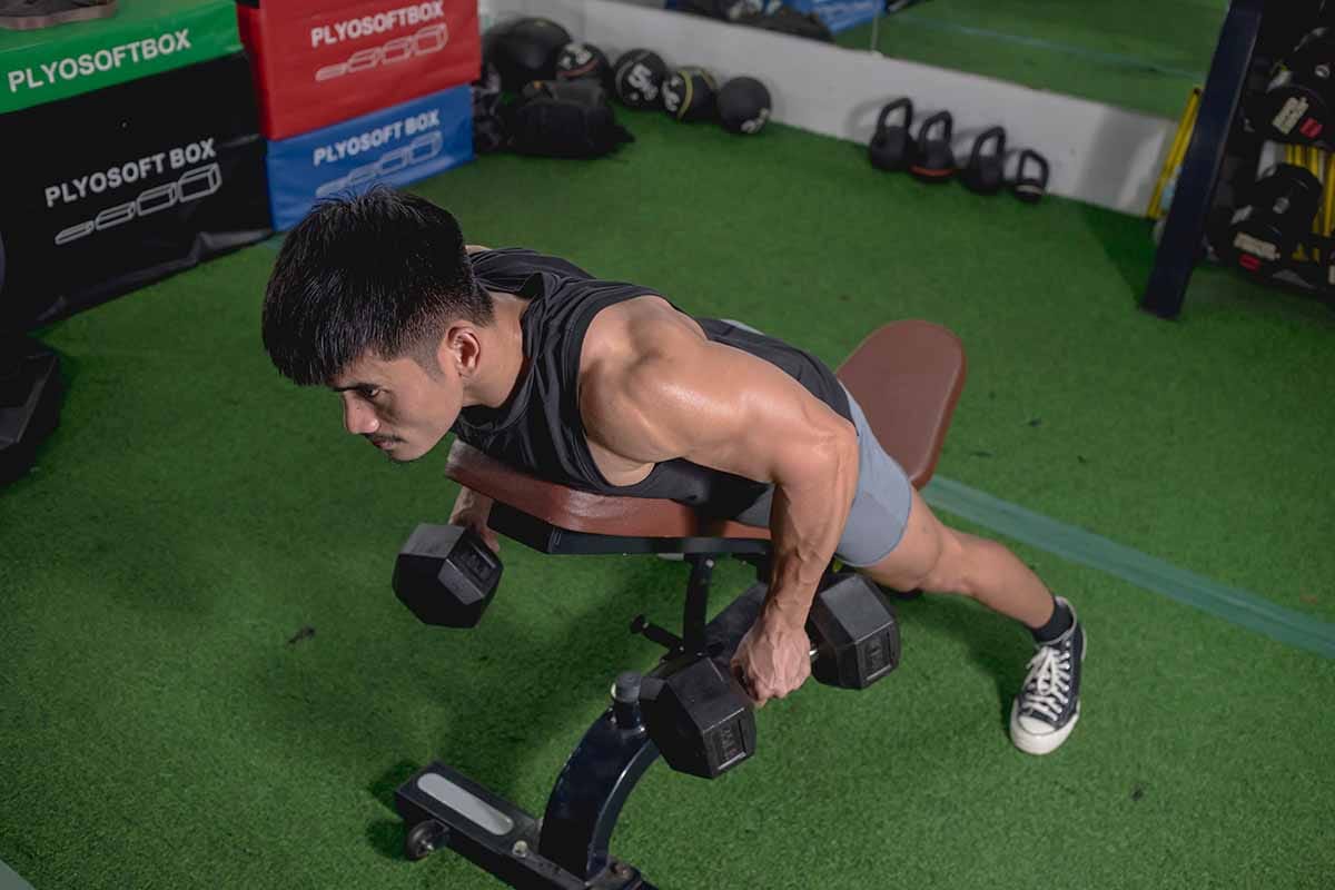 a young man doing chest supported dumbbell row at a gym