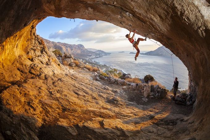 Young woman lead climbing in cave with beautiful view in background