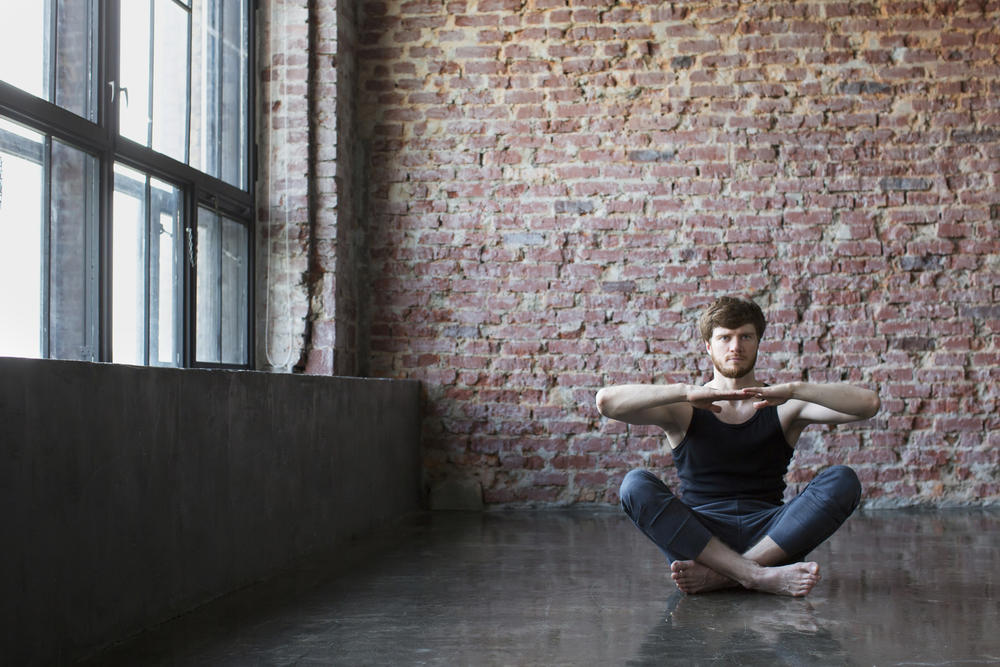 Yoga for beginners, everything you need to know-Man poses in front of brick wall next to window