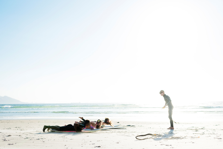 Surf instructor giving surf lessons to a group of teenagers on the beach on a sunny day