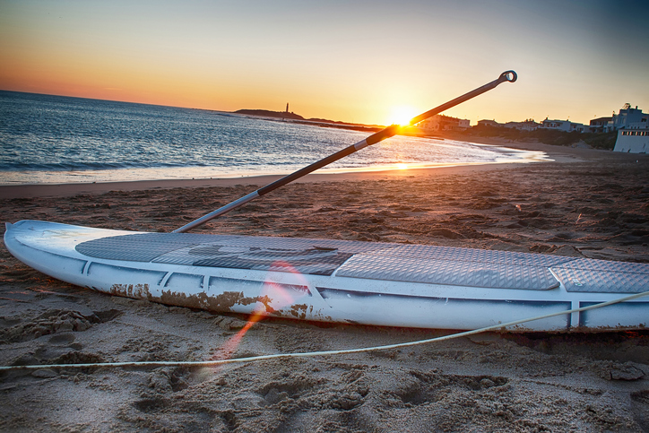 A paddle board rest on the sand at sunset. Cádiz, Spain.