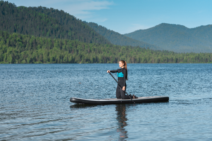 Smiling woman paddle boarding on the mountains lake